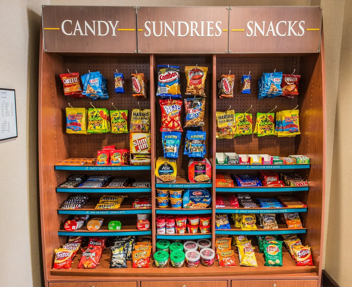 A playful and colorful interior scene that spotlights a well-stocked snack and candy display. The shelves are filled with vibrant packaging, inviting guests to indulge in treats or make quick purchases before heading out for more adventures.