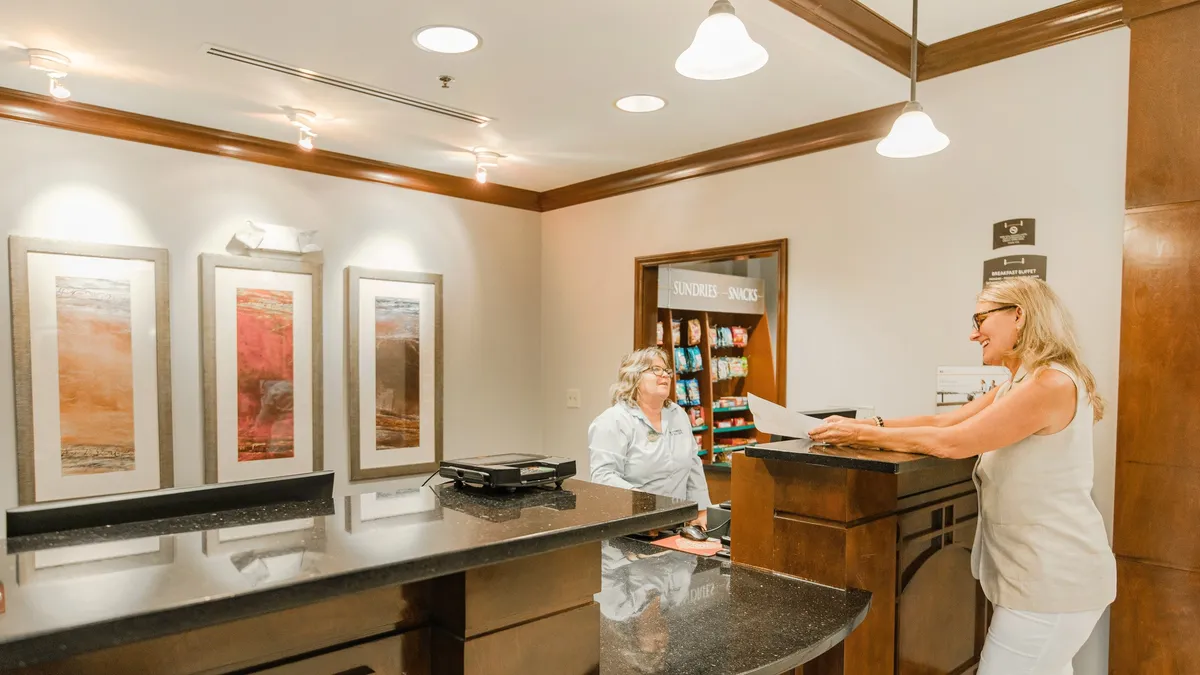 A modern, inviting interior lobby featuring a welcoming reception desk, contemporary artwork lining the walls, and a small snack area. The entry space feels bright, organized, and friendly, creating a pleasing first impression for residents and guests alike.