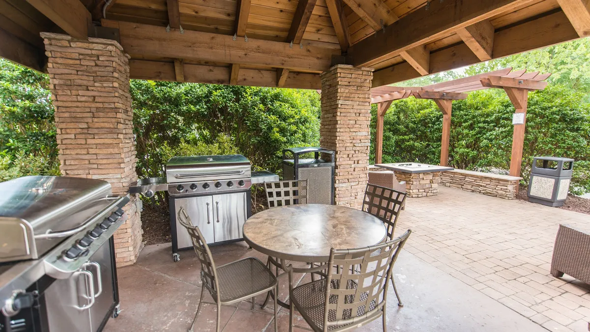 This exterior image features a welcoming grilling station and dining table set amidst lush greenery. The scene suggests an inviting outdoor space perfect for social gatherings, barbeques, and enjoying sunny days. The relaxed, communal mood encourages guests to spend time outdoors, echoing the leisurely, adventurous spirit of a beachside vacation.