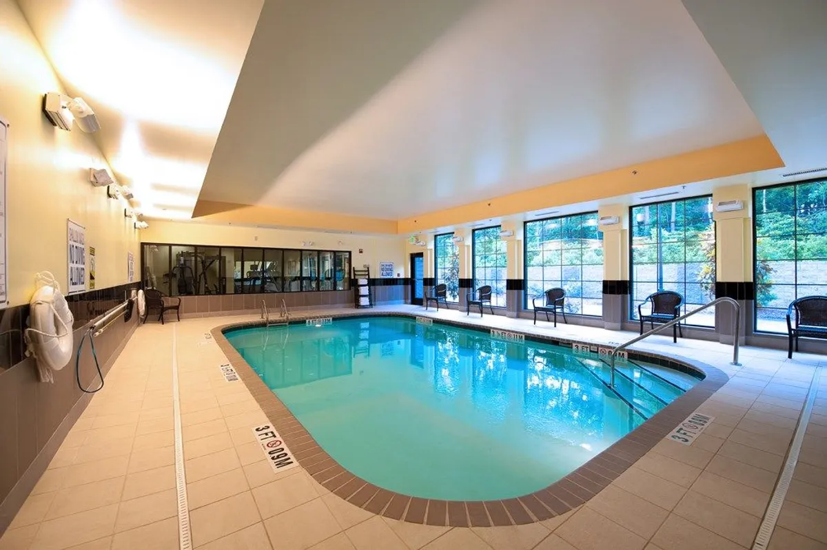 An indoor pool scene with lounge chairs positioned for poolside relaxation, large windows that connect the space visually to the outside, and a soothing, calm vibe. The image highlights leisure amenities that add value to a college visit stay.