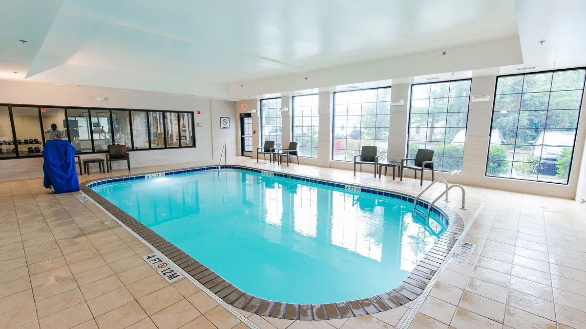 A spacious pool area with large windows letting in natural light, comfortable seating areas along the poolside, and a relaxed atmosphere ideal for gatherings or unwinding after a busy day. The scene hints at the communal amenities and openness of the property.