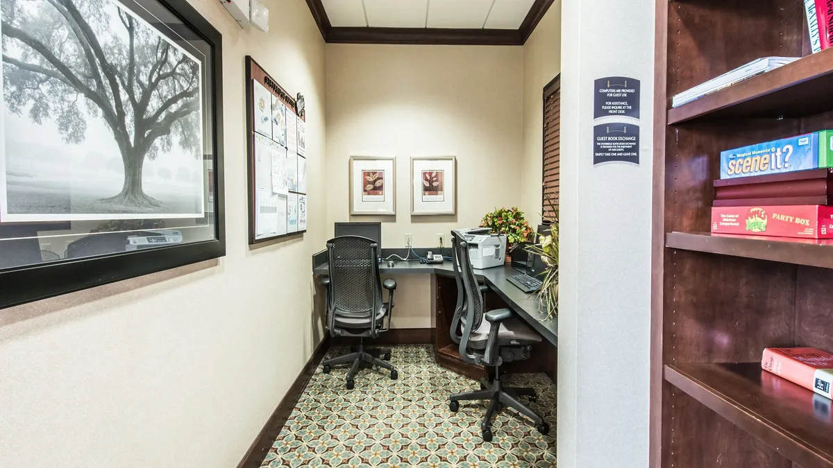 A dedicated workspace setup within a cozy environment, featuring a desk, computer, bookshelf, and framed artwork. The scene feels productive and welcoming, ideal for guests needing to work or study in a quiet setting.