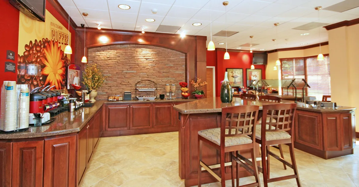 A comfortable seating area with a coffee station and a textured stone accent wall. The space is designed for casual socializing, reading, or enjoying a light meal, with soft lighting and an inviting ambiance.