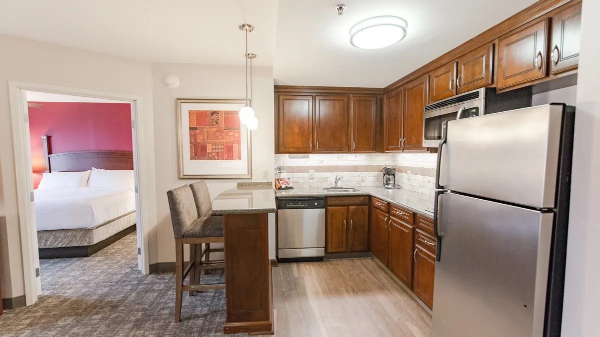 An inviting kitchen interior centered around an island with seating, complemented by sleek modern appliances and tasteful artwork on the wall. The space is arranged for both cooking and socializing, with comfortable seating that encourages guests or family to gather nearby.