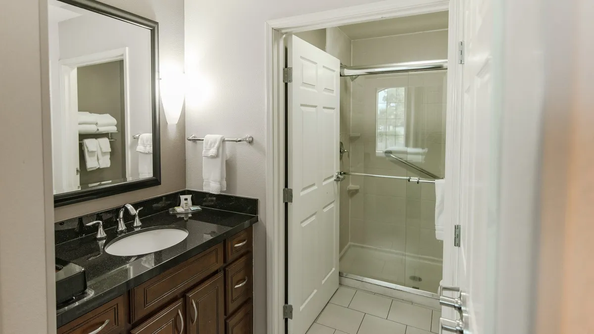 This image features a modern bathroom with a sleek vanity and sink, a mirrored wall that amplifies space and light, and a glass shower enclosure. The setting is bright, clean, and inviting, emphasizing comfort and relaxation.