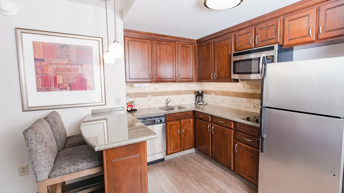 A cozy and functional kitchen scene featuring warm wooden cabinetry, a polished granite countertop, and a bar-style seating area. Modern appliances are visible, creating an inviting atmosphere suited for both meal preparation and casual dining. The space looks organized, practical, and welcoming for everyday use or entertaining guests.